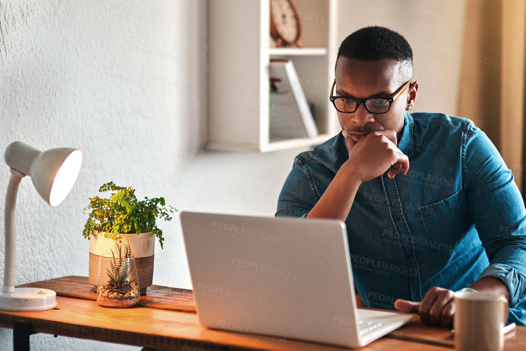 Buy stock photo Cropped shot of a handsome young businessman sitting in his home office and looking contemplative while working on his laptop