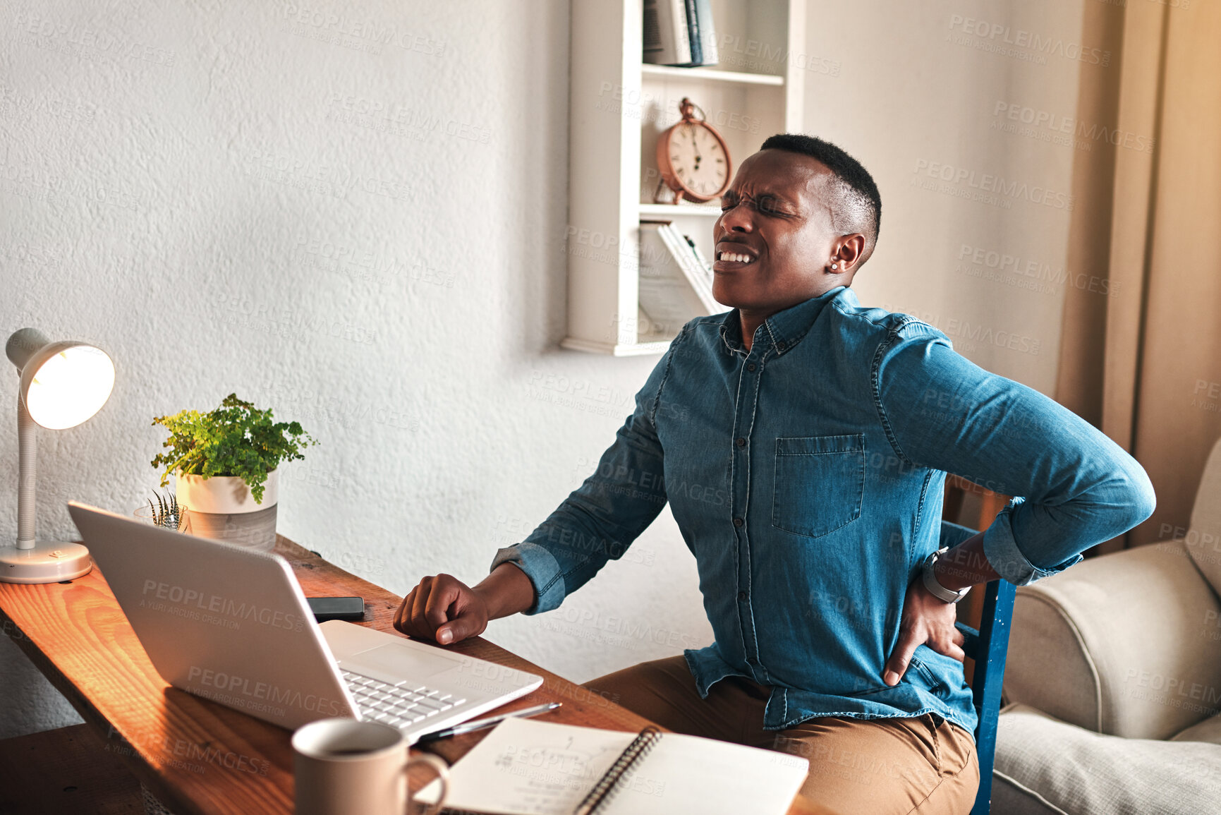 Buy stock photo Cropped shot of a handsome young businessman sitting alone in his office and suffering from back pain