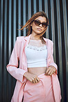 A young trendy and confident mixed race woman looking stylish while posing and spending time in the city. Fashionable hispanic woman wearing pink clothes and sunglasses 