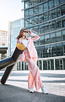 A young trendy and confident mixed race woman looking stylish while posing and spending time in the city. Fashionable hispanic woman wearing pink clothes and sunglasses standing with cool sneakers