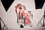 Young mixed race female posing in trendy clothing while sitting on a chair and making a call with a landline phone in a studio shoot. Confident hispanic woman in pink clothes relaxing in a chair