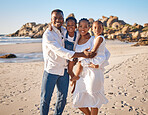 Portrait of a happy african american family with two children standing together on the beach. Loving mother and father carrying their daughter and son while spending time together on vacation