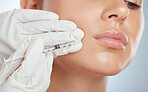 Closeup of woman getting lip fillers or botox. Young caucasian model isolated against a grey studio background with copyspace. Dermatologist injecting patient during anti ageing cosmetic procedure