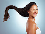 Portrait of a hispanic brunette woman with long lush beautiful hair smiling and posing against a grey studio background. Mixed race female standing showing her beautiful healthy hair