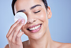 A beautiful smiling mixed race woman using a cotton pad to remove makeup during a selfcare grooming routine. Hispanic woman applying cleanser to her face against blue copyspace background