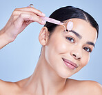 Studio Portrait of a beautiful mixed race woman using a rose quartz derma roller during a selfcare grooming routine. Young hispanic woman using anti ageing tool against blue copyspace background