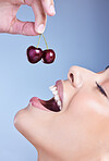 A happy smiling mixed race woman eating a cherry. Hispanic model promoting the skin benefits of a healthy diet against a blue copyspace background