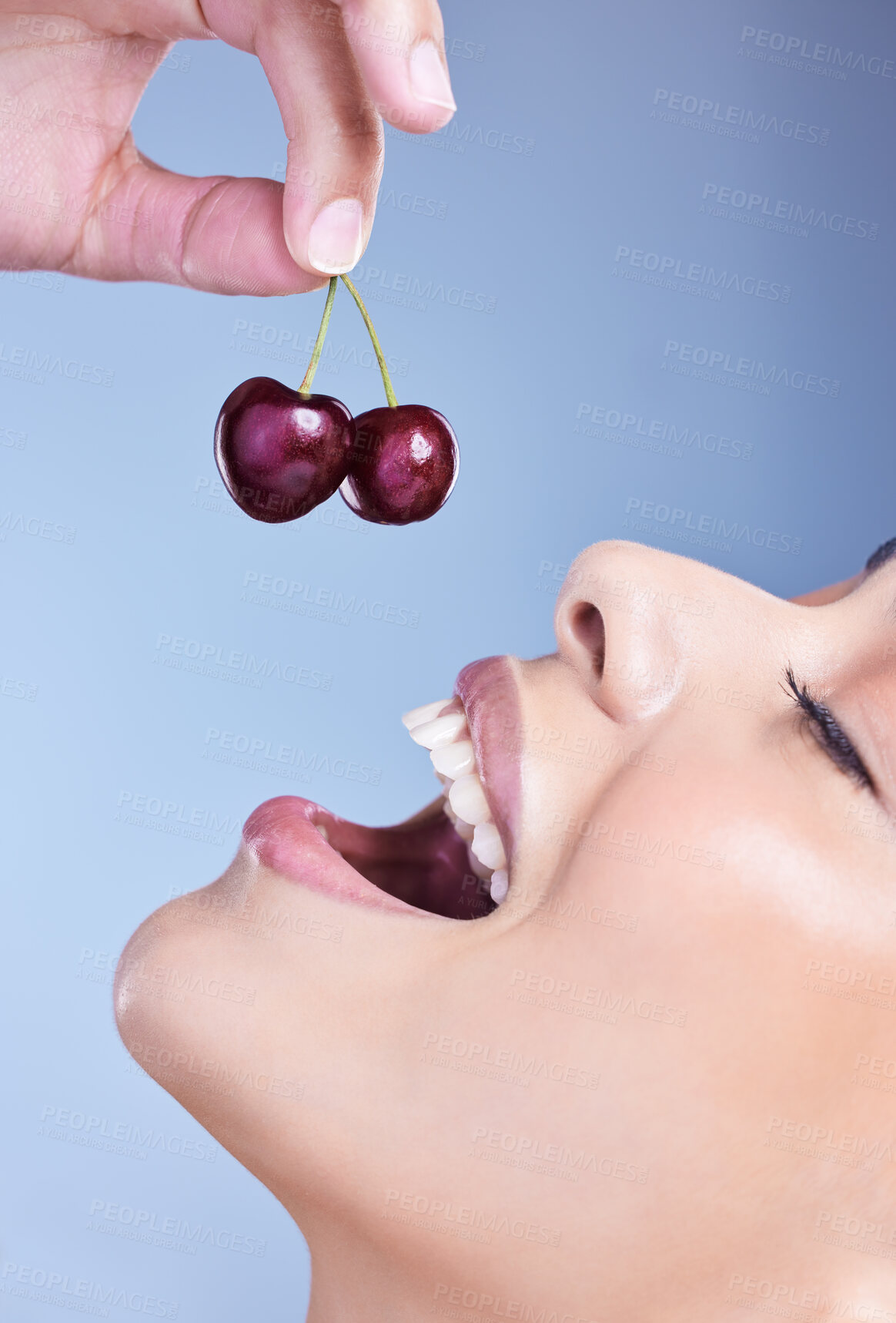 Buy stock photo Woman, smile and eating cherry in studio with closeup for healthy nutrition, digestion and benefits. Mouth, happy and female person with fruit on blue background for antioxidants, detox and vitamin c