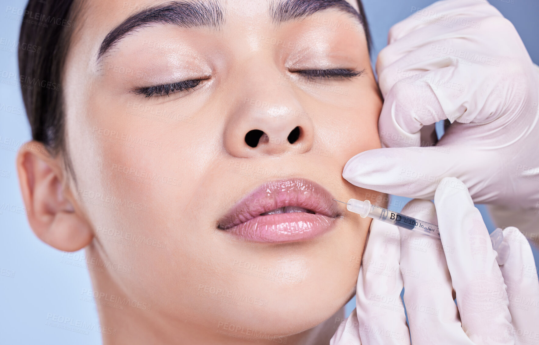 Buy stock photo Cosmetic surgery, girl and hands with filler in lips for facial transformation, beauty and change in studio. Syringe, surgeon or woman patient with injection for makeover treatment on blue background