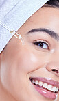 Studio Portrait of a beautiful mixed race woman applying a soothing face serum to her radiant smooth face while wearing a towel on her head. Hispanic woman with flawless skin using essential oil