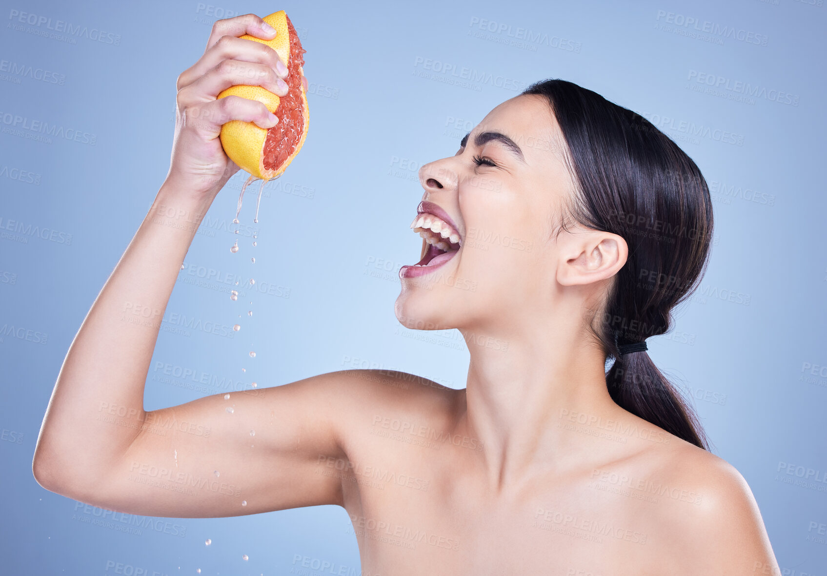 Buy stock photo Girl, grapefruit and squeeze in studio for skincare, natural benefits and organic cosmetics for vitamin c or citrus acid. Woman, fruit and scream on blue background for happiness of skin tone results