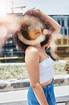 Portrait of young trendy beautiful mixed race woman with an afro smiling and posing alone outside. Hispanic woman wearing sunglasses and feeling happy. Fashionable african american woman in the city