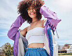 Portrait of young trendy beautiful mixed race woman with an afro smiling and posing alone outside. Hispanic woman wearing sunglasses and feeling happy. Fashionable African American woman in the city