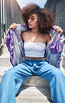 Young trendy beautiful mixed race woman with an afro sitting alone and posing alone outside. Hispanic woman with curly hair, sunglasses and hipster clothes. Fashionable African American woman in city