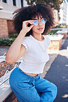 Young stylish mixed race woman with curly natural afro hair wearing trendy glasses outside. One female only looking carefree, cool and confident. Happy fashionable hispanic woman relaxing in the city