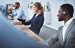 Happy young caucasian call centre telemarketing agent talking on a headset while working on computer alongside colleagues in an office. Confident friendly female consultant operating helpdesk for customer service and sales support