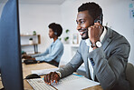 Happy young african american call centre telemarketing agent talking on a headset while working on computer in an office. Confident friendly male consultant operating helpdesk for customer service and sales support