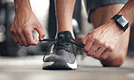 Closeup of one mixed race man tying his shoelaces while exercising in a gym. Guy fastening sneaker footwear for a comfortable fit and to prevent tripping during a training workout in a fitness centre