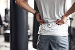 Closeup of one mixed race man holding his sore lower back while exercising in a gym. Guy suffering with painful spine injury from fractured joint and inflamed muscles during workout. Struggling with stiff body cramps causing discomfort and strain