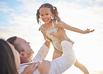 Cute mixed race girl being lifted into the air by her mixed race father while her mother watches. Adorable daughter and her parents spending time together by the ocean at sunset. Family bonding