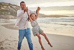 Cute little girl swinging while holding hands with her father. Young dad walking hand in hand with his daughter and lifting her while walking on the beach. Family fun in the summer at sunset