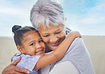 Smiling adorable little mixed race girl hugging her grandmother while bonding with her at home. Beautiful hispanic mature woman showing love and affection to her granddaughter in the living room