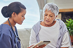 A hispanic senior woman in on a cosy sofa and her female nurse in the old age home and using a digital tablet. Mixed race young nurse and her patient talking in the lounge