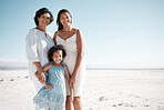 Smiling mixed race family standing together on a beach with copyspace. Happy hispanic grandmother bonding with granddaughter over weekend. Adorable little girl enjoying free time with single mother