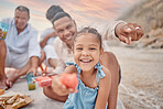 Portrait of a little hispanic girl having a snack while on a picnic with her family at the beach. Mixed race girl having fun with her family and having snacks