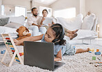 Closeup of a little cute girl using a laptop and wireless headphones while laying on the floor in the lounge. Hispanic girl using a wireless device to do her homework in the living room