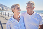 A happy mature caucasian couple enjoying fresh air on vacation at the beach. Smiling retired couple getting a cardio workout while walking outside