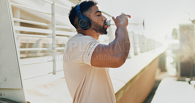 Buy stock photo Fitness, drinking water and man in city with headphones, break and hydration in training. Athlete, bottle or music on run for workout, healthy body or rest on sidewalk with nutrition or care in sport