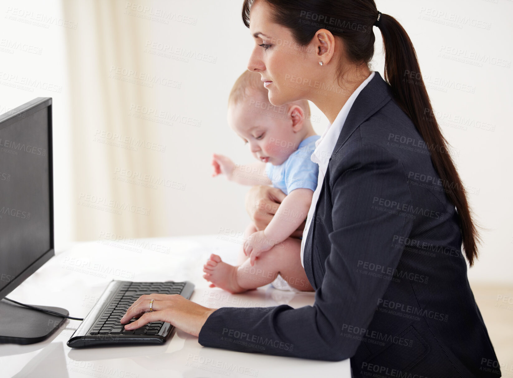 Buy stock photo Young working mother holding a baby while working on her computer