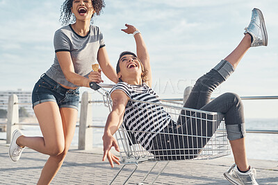 Buy stock photo Friends, women and laugh with trolley outdoor for freedom, bonding or transport ride of beach travel in summer. People, girls and smile with shopping cart for playful game, funny and fun by ocean