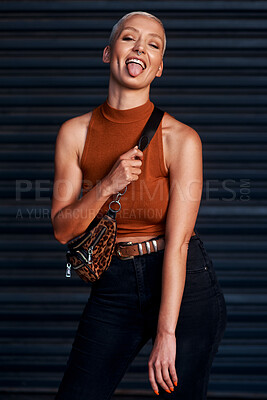 Buy stock photo Cropped shot of an attractive young woman sticking out her tongue while standing against a dark background