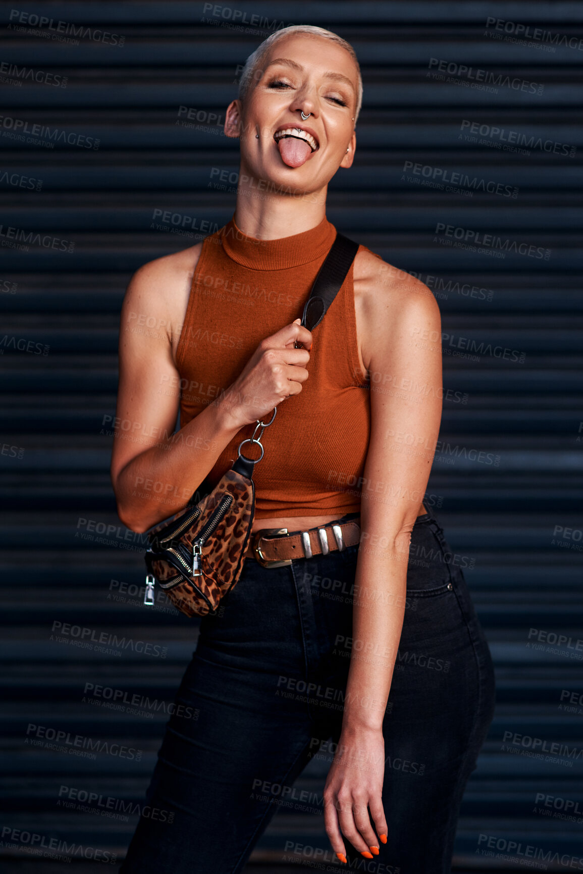 Buy stock photo Cropped shot of an attractive young woman sticking out her tongue while standing against a dark background