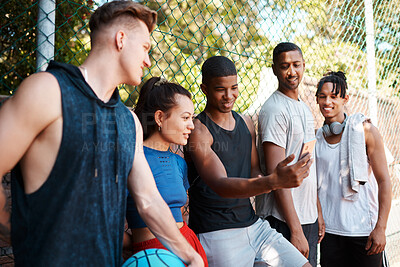 Buy stock photo Shot of a group of sporty young people looking at something on a cellphone while standing along a fence outdoors