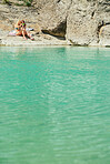 Happy friends on holiday taking selfies on a cellphone sitting by a lake. Two women on holiday wearing bikinis taking selfies on a cellphone before swimming in a lake