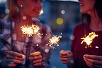 Cheerful friends playing with sparklers at night on holiday together. Happy friends on holiday playing with sparklers outside in the city. Two friends on holiday celebrating playing with sparklers