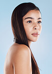 One beautiful young hispanic woman with healthy skin and sleek long hair posing against a blue studio background. Mixed race model with flawless complexion and natural beauty