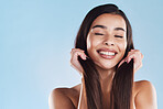 One beautiful young hispanic woman touching her sleek, silky and healthy long hair while smiling against a blue studio background. Confident and happy mixed race model with flawless complexion and natural beauty