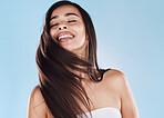 One beautiful young hispanic woman with healthy skin tossing her sleek long hair against a blue studio background. Happy mixed race model with flawless complexion and natural beauty