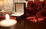 Closeup of romantic engagement ring box, fresh red roses and candles in an empty room at night. Getting ready and prepared for  surprise proposal. Loving couple popping the question with sweet gesture