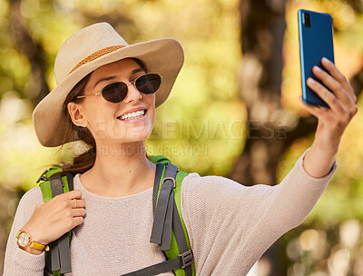 Buy stock photo Nature, phone selfie and woman hiking with hat, sunglasses and smile, adventure in forest or woods in summer. Freedom, peace and exercise, a walk in the trees to relax mindset and enjoy weekend time.