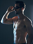 Sports, fitness and body of swimmer in studio with goggles  for wellness, exercise and swimming training. Workout, motivation and man athlete on dark background with muscle, strong body and tattoo