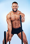 Fitness, man and portrait in battle rope for intense workout, exercise or training against blue studio background. Strong and fit muscular male model in roping practice for exercising endurance