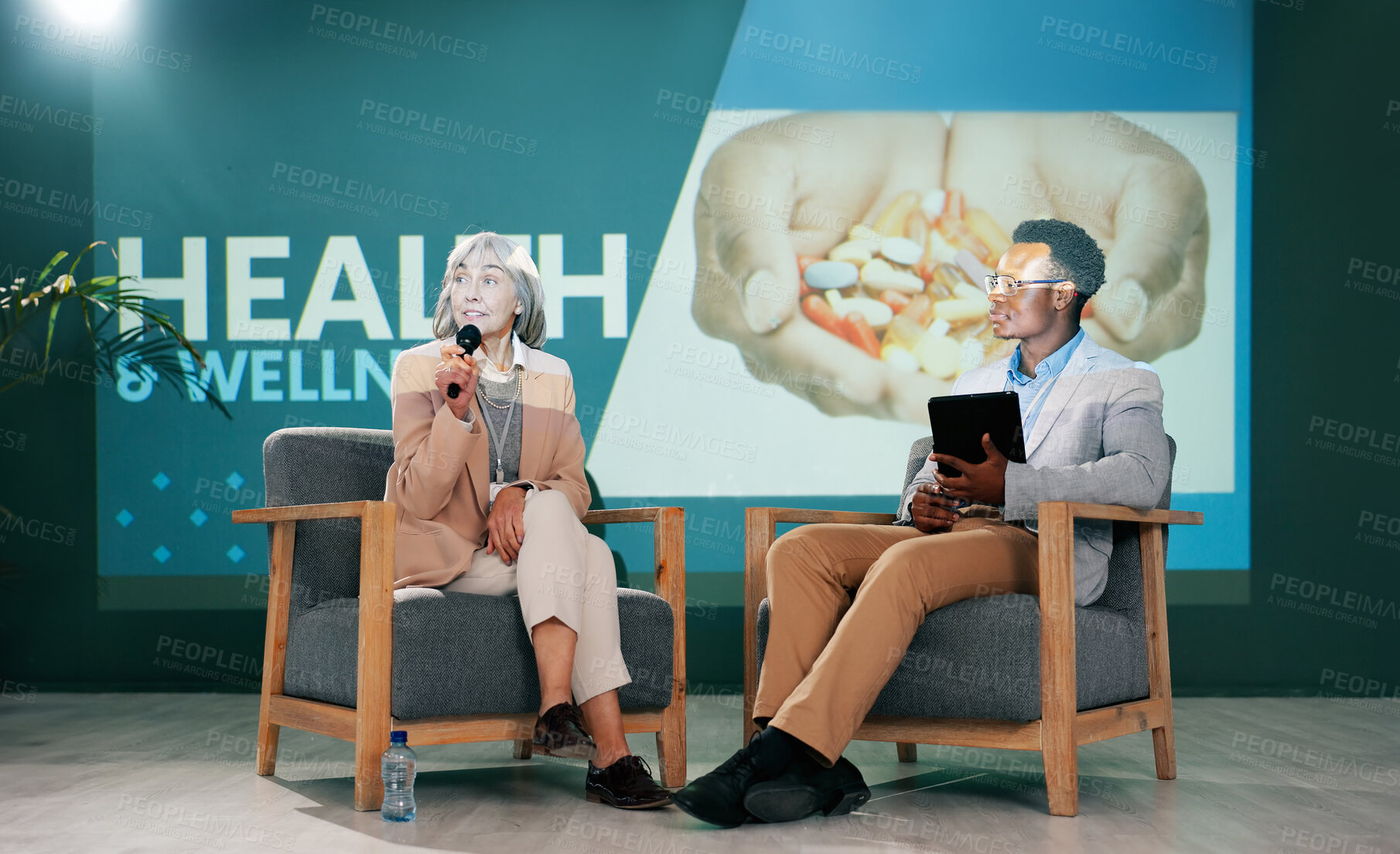 Buy stock photo Speaker, health seminar and speech of woman on stage with host on mic and tablet at event. Workshop, talk and conference presentation on wellness, medicine or medical innovation of drugs with guest