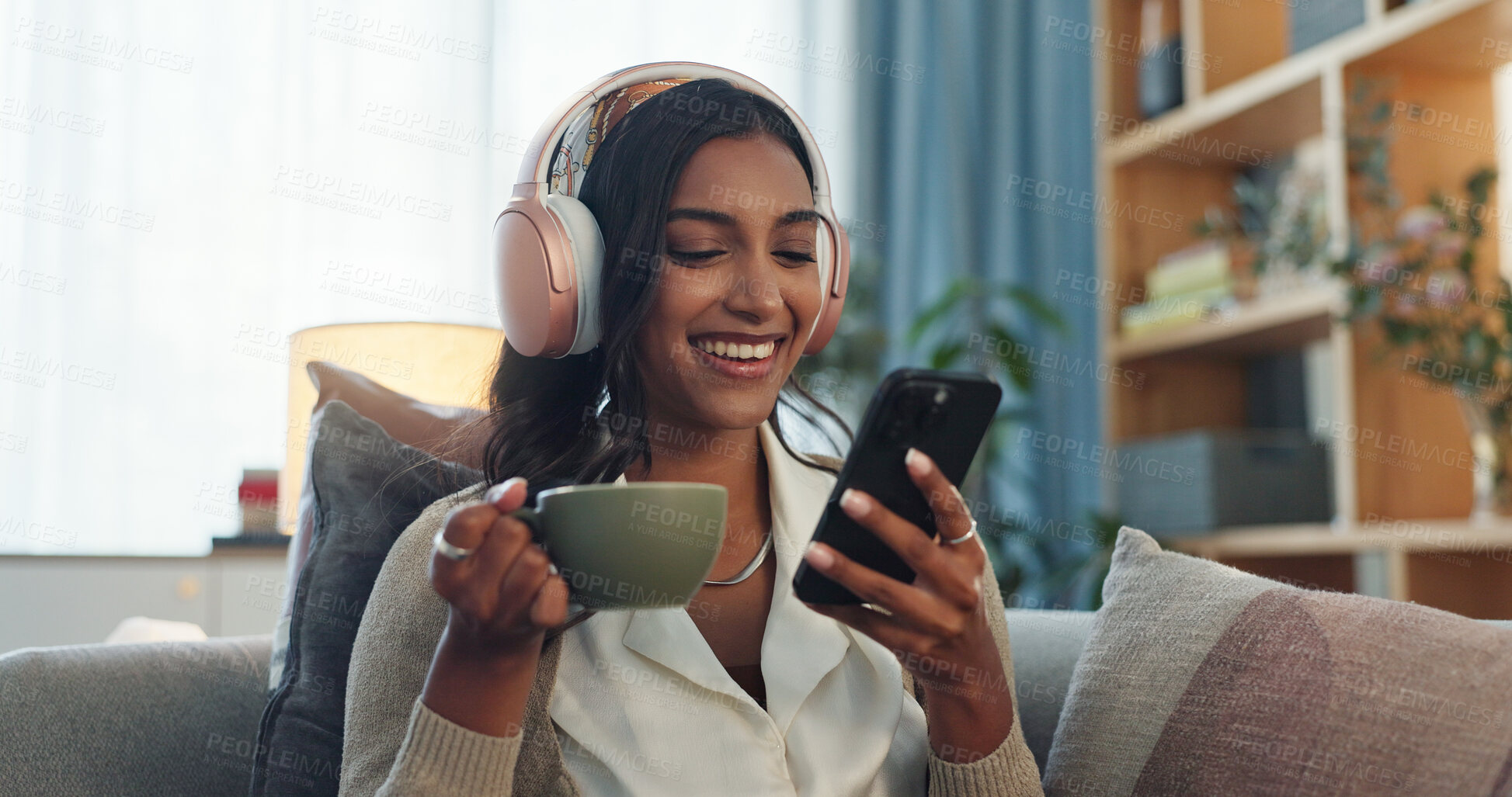 Buy stock photo Headphones, indian woman and cellphone for social media in home, laugh and music in living room. Coffee, relax and online audio streaming or podcast for break, chai tea or happy female person on sofa