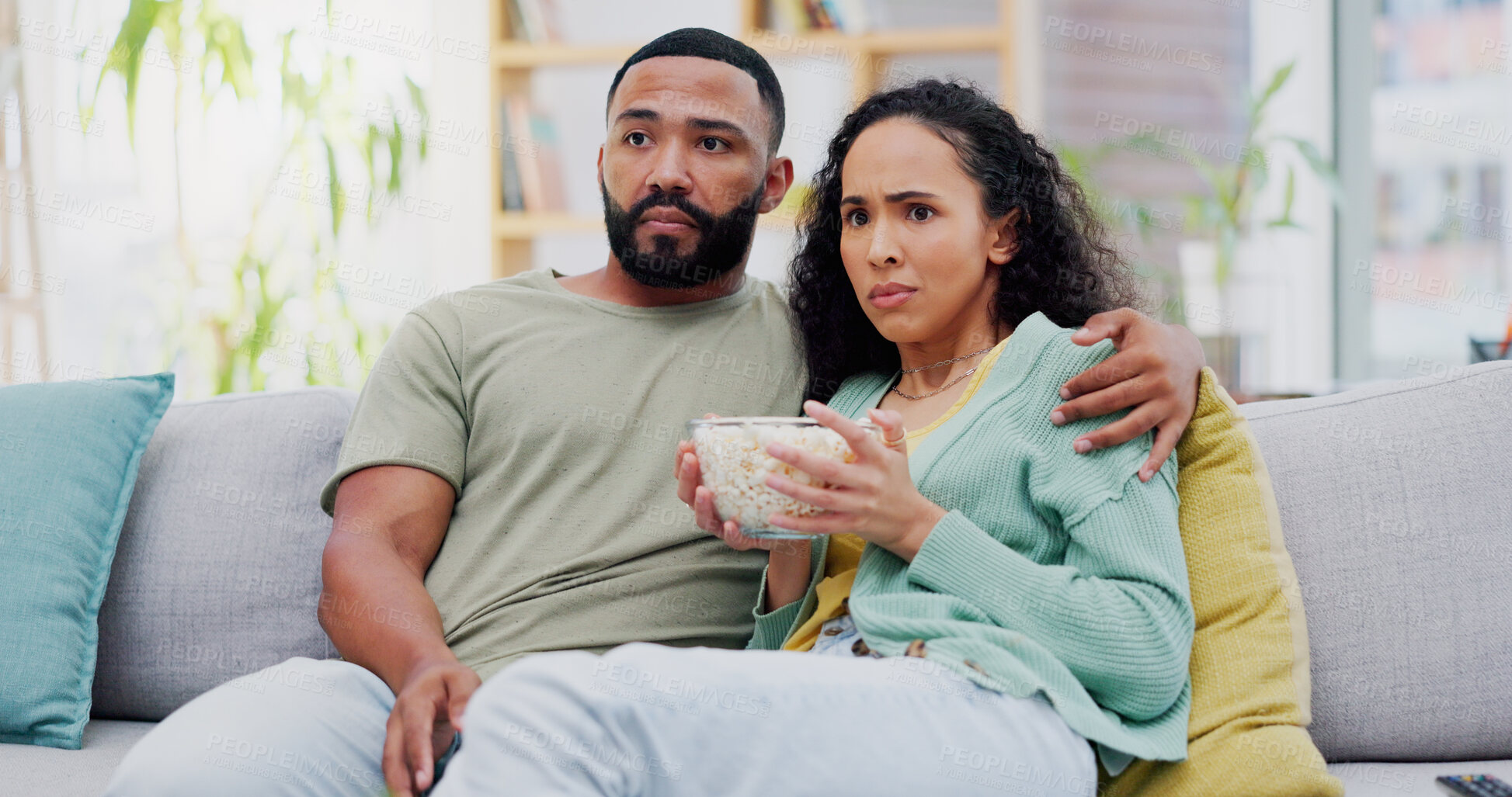 Buy stock photo Couple, scared and watching tv on sofa with popcorn in home for horror film, streaming and hug in living room. Man, woman and subscription with snack, fear and eating on couch for movie date in house