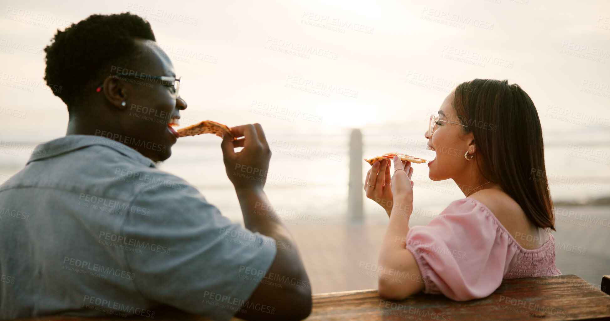 Buy stock photo Couple, pizza and relax with eating at beach for bonding, relationship or romance with summer sunset. Interracial people, love and food at ocean for support, trust and loyalty on holiday vacation